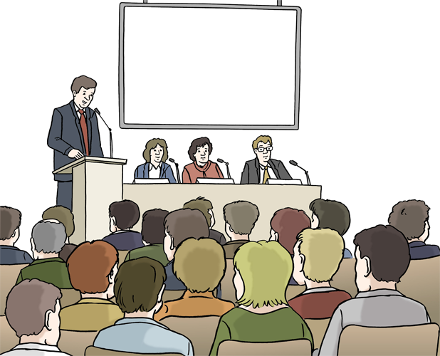 Eine Person spricht am Rednerpult vor Publikum. Dahinter sitzen drei Personen an einem Tisch mit Mikrofon